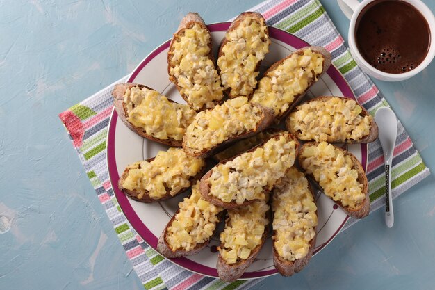 Toasts faits maison au four avec poulet, fromage, ananas et ail ainsi qu'une tasse de café sur fond bleu clair. Vue d'en-haut. Fermer