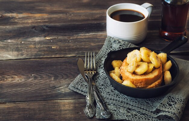 Toasts français avec des bananes frites dans une poêle en fer sur bakground en bois rustique.