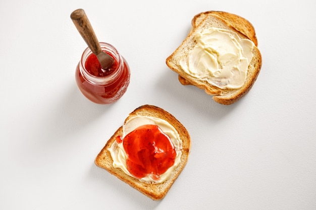 Toasts en gros plan avec confiture de fraises et pain et pot sur le tableau blanc