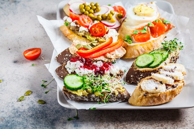 Toasts ouverts avec différentes garnitures sur fond gris-brun