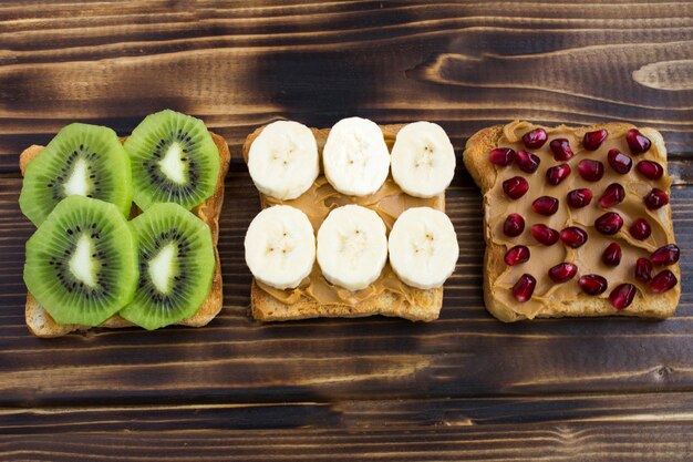 Toasts avec pâte d'arachide et fruits sur le fond en bois marron