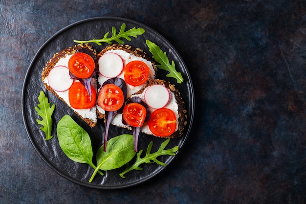 Toasts sains avec fromage à la crème, tomates cerises et épinards sur plaque noire