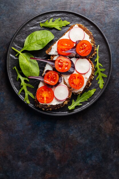 Toasts sains avec fromage à la crème, tomates cerises et épinards sur plaque noire