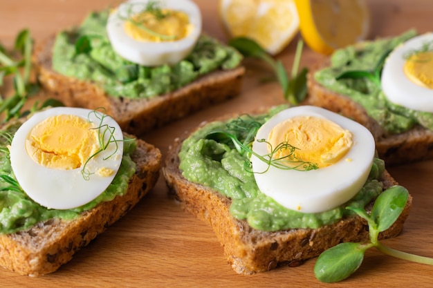 Toasts sains avec pain de grains entiers, avocat et œuf à la coque sur planche de bois.