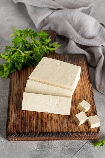 tofu au fromage frais de soja avec persil sur une planche sur fond gris. produit végétalien.