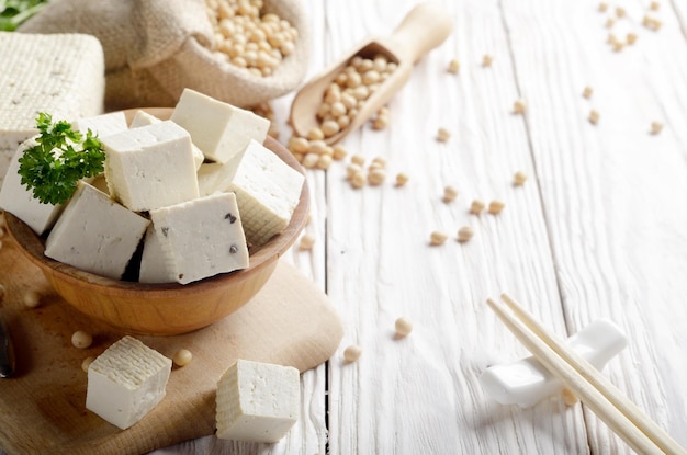 Tofu caillé de soja dans un bol en bois et dans un sac de chanvre sur une table de cuisine en bois blanc Autre substitut non laitier pour le fromage Place pour le texte