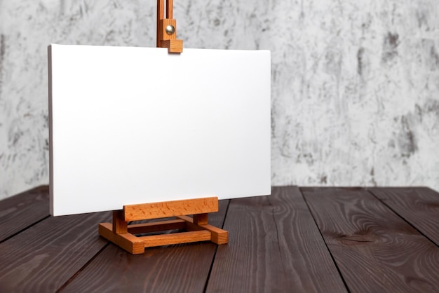 Une toile blanche étirée sur un sous-cadre et un chevalet sur une table en bois brun Mockup