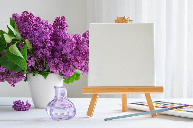 Toile vierge sur chevalet peinture aquarelle pinceau pour peinture et fleurs lilas sur table