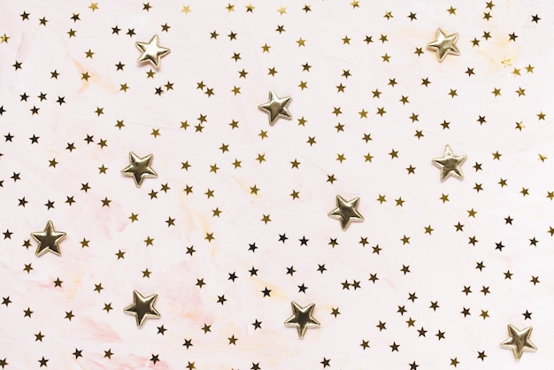 Étoiles de confettis dorés à la mode sur fond rose.