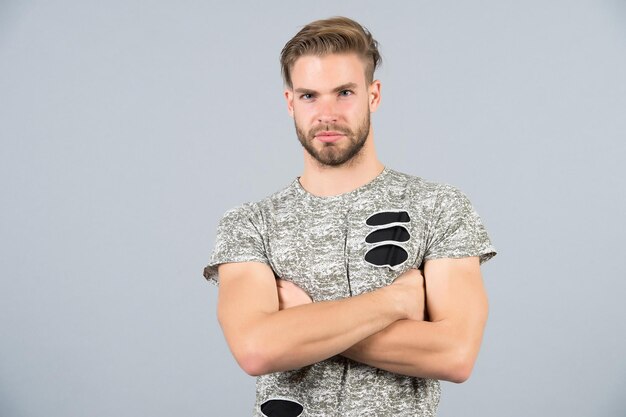 Toilettage, concept de beauté masculine. Homme en tshirt avec les mains jointes sur fond gris. Salon de coiffure, salon de coiffure. Mode, style, tendance. Macho avec visage barbu et cheveux élégants, coupe de cheveux, espace de copie