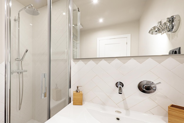 Photo toilettes en carrelage blanc avec robinets design et douche à l'italienne avec cloison en verre et miroir sans cadre au mur