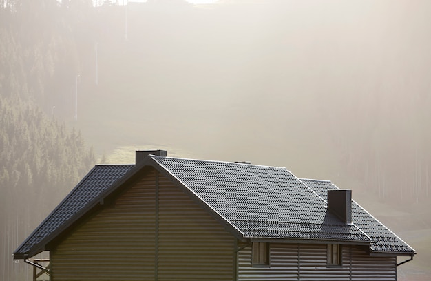 Toit de chalet avec murs de parement, toit en bardeaux bruns et hautes cheminées dans une zone écologique sur un paysage brumeux