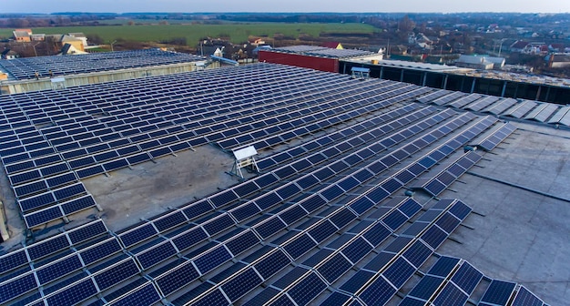 Toit d'entrepôt utilisé pour l'installation de nombreuses centrales solaires Personnes sur le sol parmi les panneaux solaires Village et champ agricole à l'arrière-plan