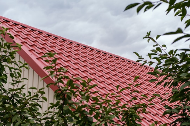 Un toit fait de tuiles métalliques rouges avec une cheminée contre un ciel nuageux.