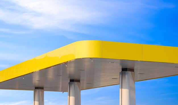 Un toit jaune moderne avec des colonnes de station-service sur un fond bleu.