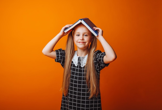 Un toit de livre au-dessus de votre tête Une petite fille tient un manuel sur la tête Une petite fille avec un livre sur fond orange