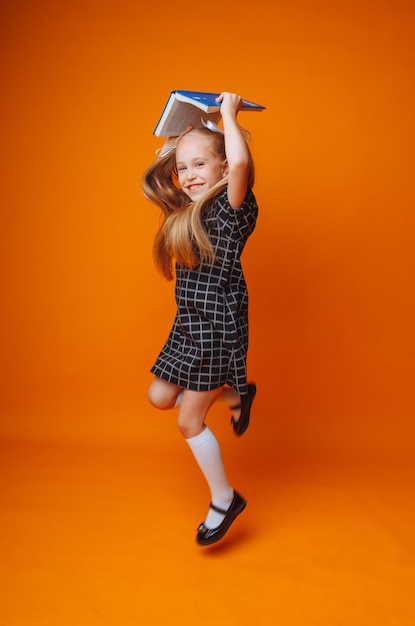 Un toit de livre au-dessus de votre tête Une petite fille tient un manuel sur la tête Une petite fille avec un livre sur fond orange