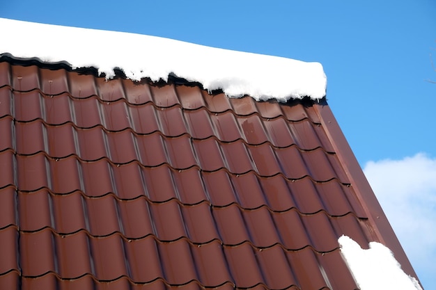 Le toit d'une maison de campagne en carreaux métalliques bruns avec de la neige dans une journée ensoleillée de printemps sous un ciel bleu sans nuages