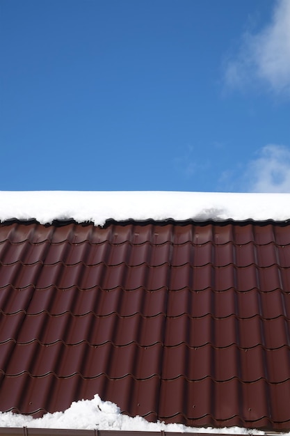 Photo le toit d'une maison de campagne en carreaux métalliques bruns avec de la neige dans une journée ensoleillée de printemps sous un ciel bleu