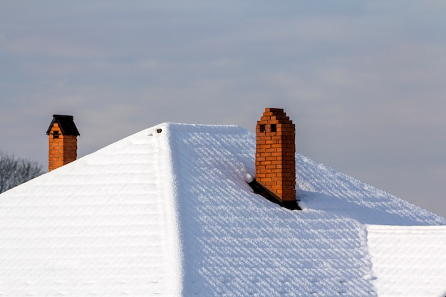 Toit de la maison avec cheminées en briques recouvertes de neige en hiver