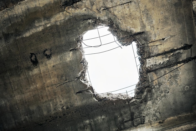 Toit de maison endommagée abandonnée vintage avec trou dans le plafond donnant sur un ciel nuageux. Mur de béton effondré avec trou dans un bâtiment industriel abandonné, gros plan