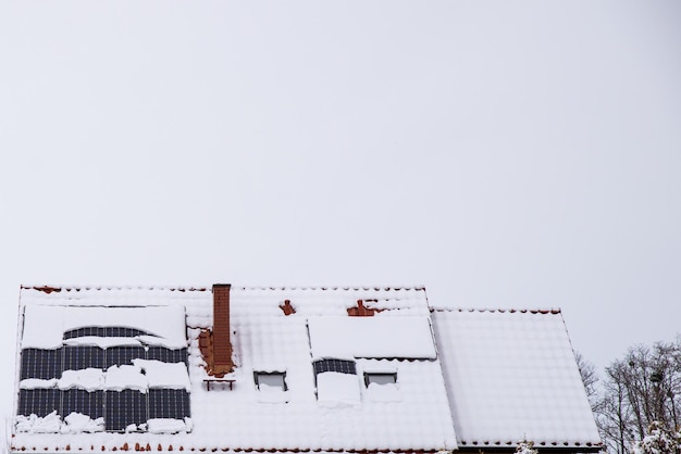 Photo le toit d'une maison avec des panneaux solaires couverts de neige.