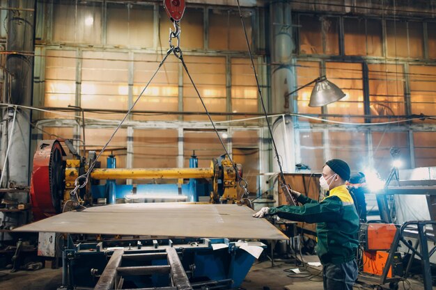 Tôle de levage de travailleur avec palan à chaîne de grue avec télécommande et crochet à l'usine industrielle.