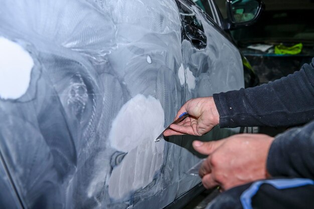 Tôlier modelant au mastic la carrosserie d'une voiture