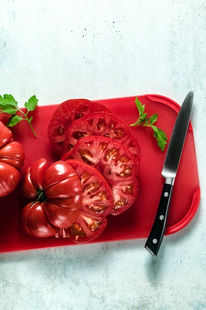 Tomate Beefsteak en tranches sur une planche à découper rouge et un couteau. cuisiner des repas d'été sains