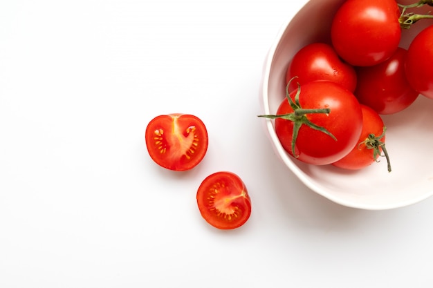 Tomate cerise fraîche dans un bol blanc sur fond blanc. Concept d'aliments crus et de légumes