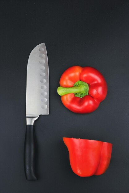 Une tomate coupée en deux moitiés avec un couteau bien aiguisé Un couteau bien aiguisé et une tomate sur fond noir sur une surface noire