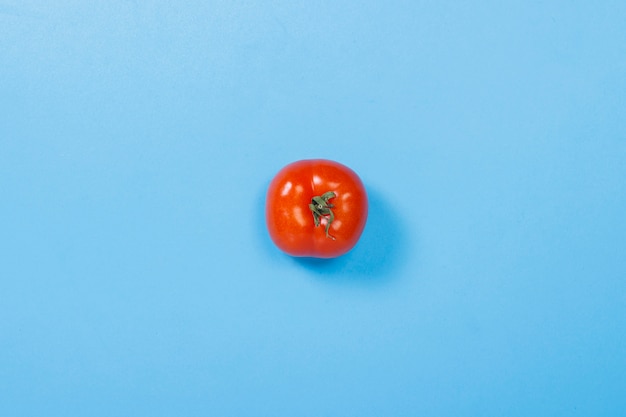 Tomate sur fond bleu. Concept de vitamines, été, petit déjeuner. Mise à plat, vue de dessus.