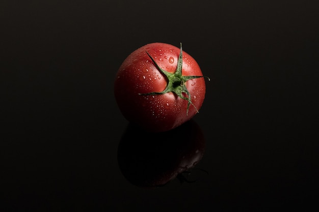 Tomate fraîche humide sur fond noir avec reflet