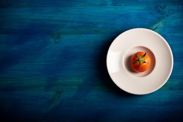 Une tomate sur une plaque blanche sur fond bleu - vue de dessus