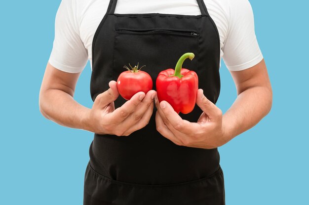 Tomate et poivron entre les mains d'un chef masculin isolé sur fond bleu