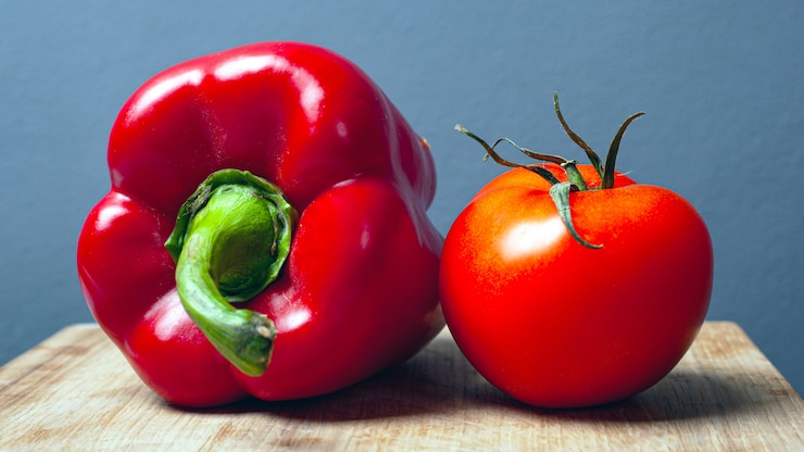 Photo tomate et poivron rouge doux sur une plaque de bois sur un fond gris. légumes frais et sains.
