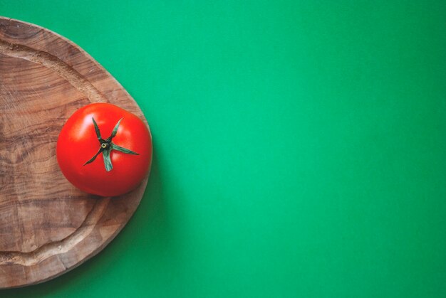 Tomate rouge sur une planche à découper en bois sur une surface verte. Pris par une caméra d'en haut.