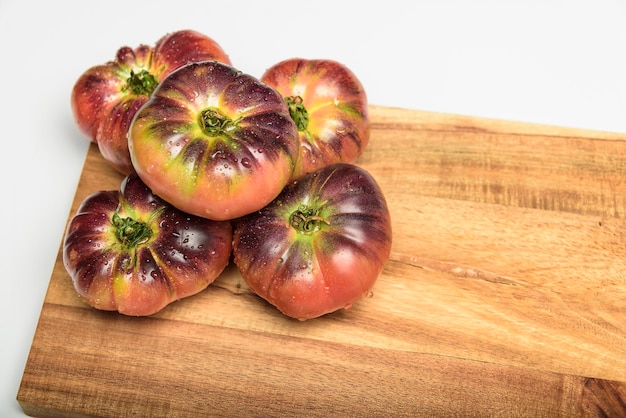 Tomate tigrée sur une planche à découper avec des feuilles de basilic sur fond en bois Espace de copie Tomate fraîche gaspillée pour la cuisson Tomate avec des gouttelettes d'eau