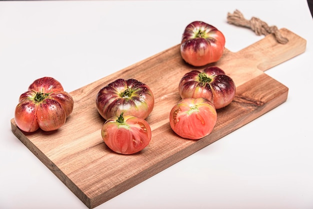 Tomate tigrée sur une planche à découper avec des feuilles de basilic sur fond en bois Espace de copie Tomate fraîche gaspillée pour la cuisson Tomate avec des gouttelettes d'eau