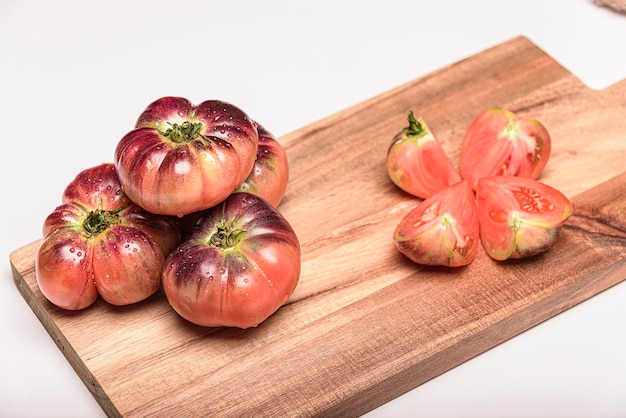 Tomate tigrée sur une planche à découper avec des feuilles de basilic sur fond en bois Espace de copie Tomate fraîche gaspillée pour la cuisson Tomate avec des gouttelettes d'eau