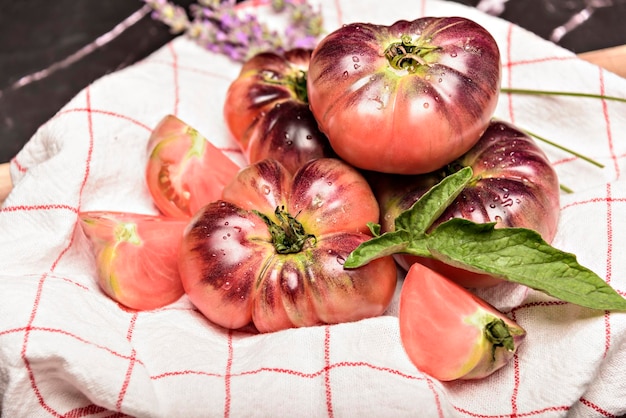 Tomate tigrée sur une planche à découper avec des feuilles de basilic sur fond de bois Tomate fraîche gaspillée pour la cuisson Tomate avec des gouttelettes d'eau