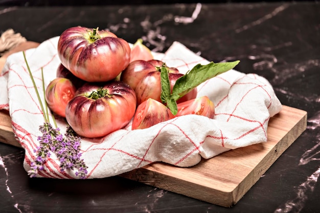 Tomate tigrée sur une planche à découper avec des feuilles de basilic sur fond de bois Tomate fraîche gaspillée pour la cuisson Tomate avec des gouttelettes d'eau