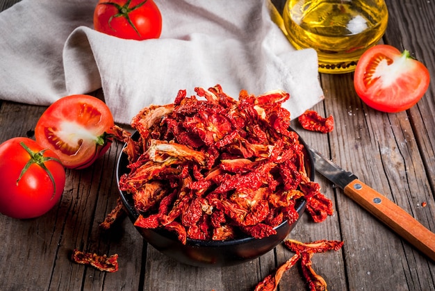 Tomates biologiques séchées maison, chips de tomates croustillantes, sur une vieille table en bois rustique avec des tomates fraîches et de l'huile d'olive.