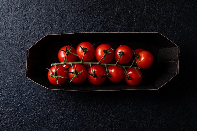 Tomates cerises sur une branche dans un paquet sur fond sombre