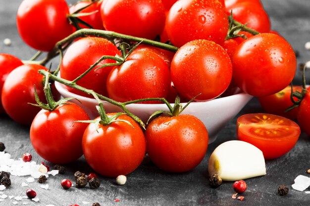 Tomates cerises sur branche et épices sur fond sombre