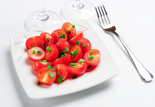 Tomates cerises décorées d'oignons verts. Sur une assiette carrée blanche.