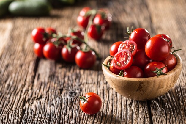 Tomates cerises fraîches dans un bol en bois sur une vieille table en chêne.