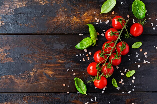 Tomates cerises fraîches, feuilles de basilic, fromage mozzarella et huile d'olive sur fond de bois ancien. Ingrédients de la salade Caprese. Mise au point sélective.