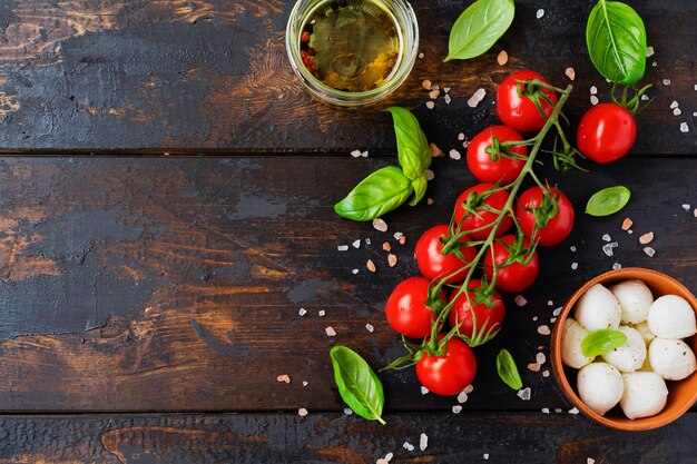 Tomates Cerises Fraîches, Feuilles De Basilic, Fromage Mozzarella Et Huile D'olive Sur Fond De Bois Ancien. Ingrédients De La Salade Caprese. Mise Au Point Sélective.