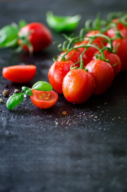 Tomates cerises fraîches sur fond noir au basilic, épices.